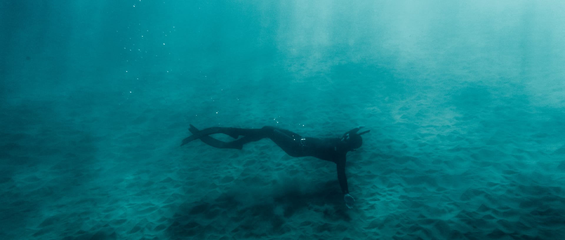 Christina Gindl trägt lässt sich am Meeresboden beim Freediving im Neoprenanzug treiben