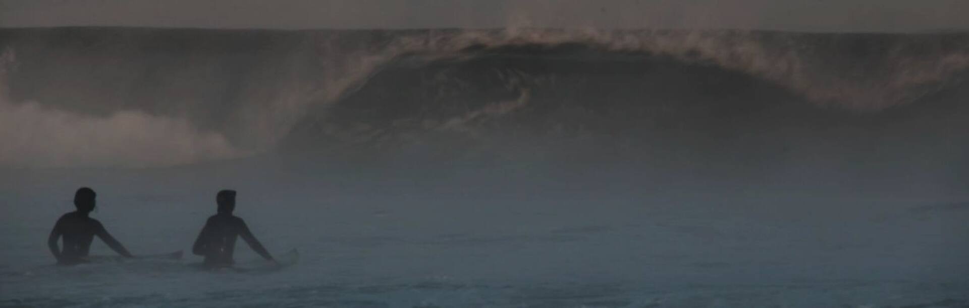 Lena Kemna und Christina Gindl sitzen auf Surfboards im Wasser vor einer Welle