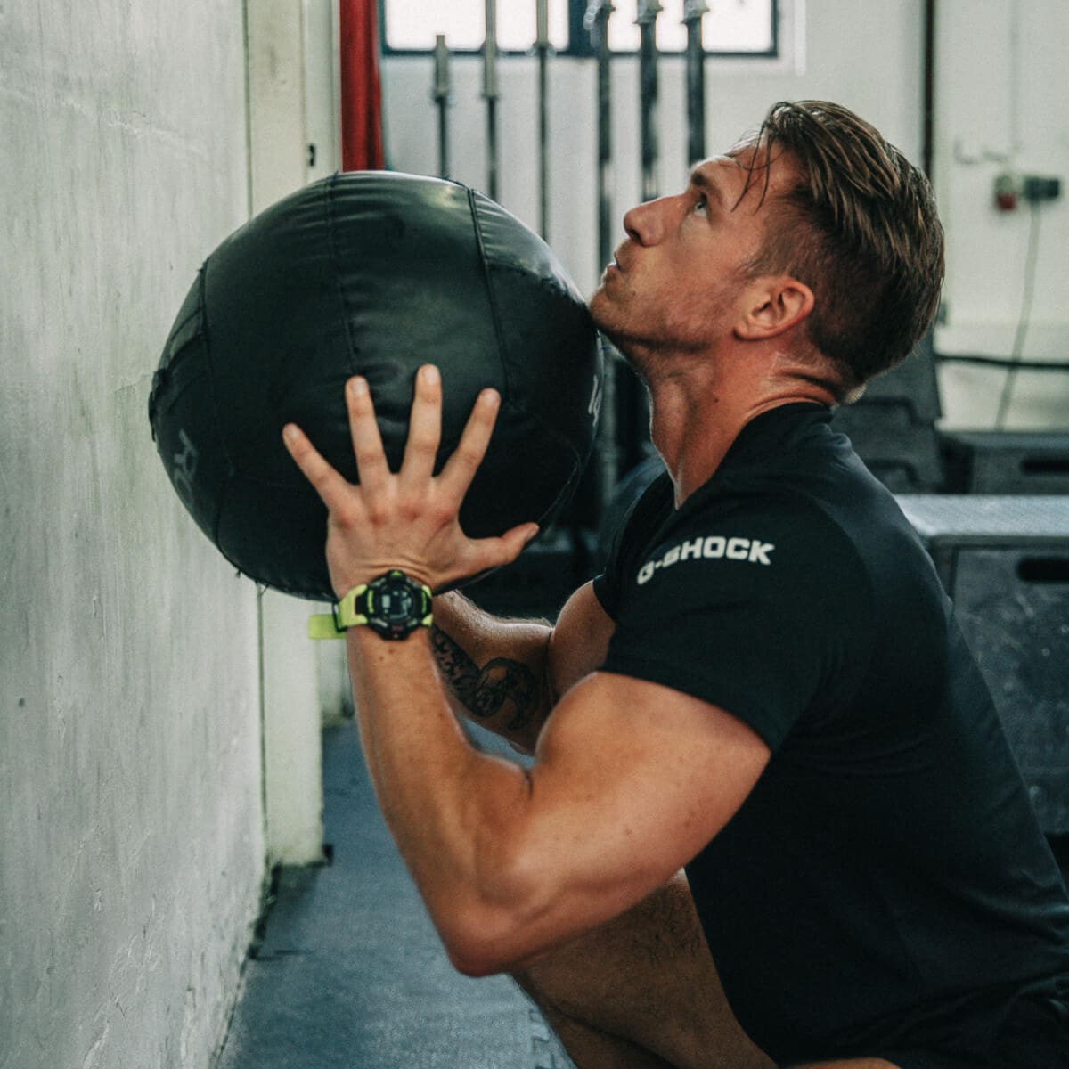 Ein Mann ist im Fitnessstudio mit einem Medizinball in der Hocke. Beim Trainig trägt er die GBD-H2000 am Handgelenk