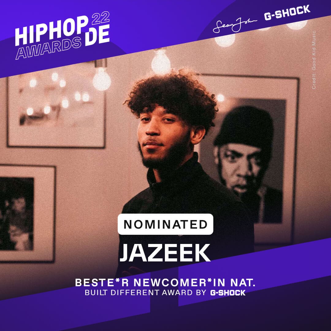 Rapper Jazeek war als bester Newcomer national nominiert, er steht in schwarzem Rollkragen-Pullover vor einem Bild von Rapper Jay-Z.