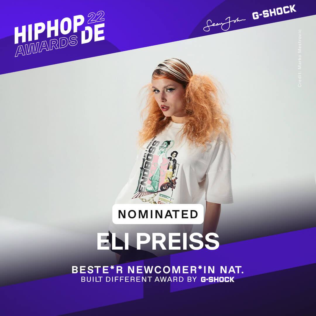 Rapperin Eli Preiss steht mit weißem, bedrucktem Shirt vor einer weißen Wand und war als beste Newcomerin national nominiert