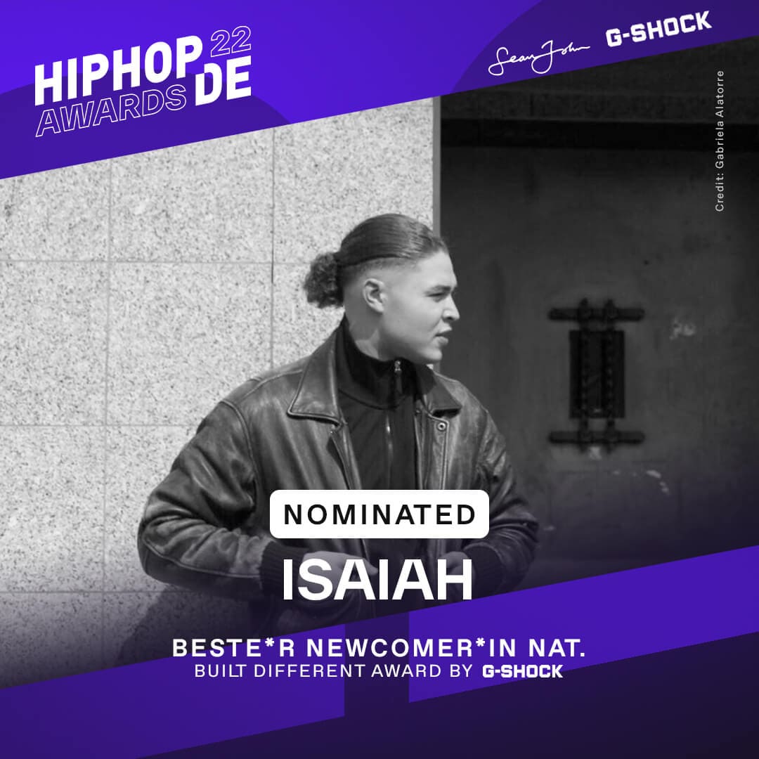 Rapper Isaiah steht mit schwarzer Lederjacke vor einem grauem Gebäude und war als bester Newcomer national nominiert