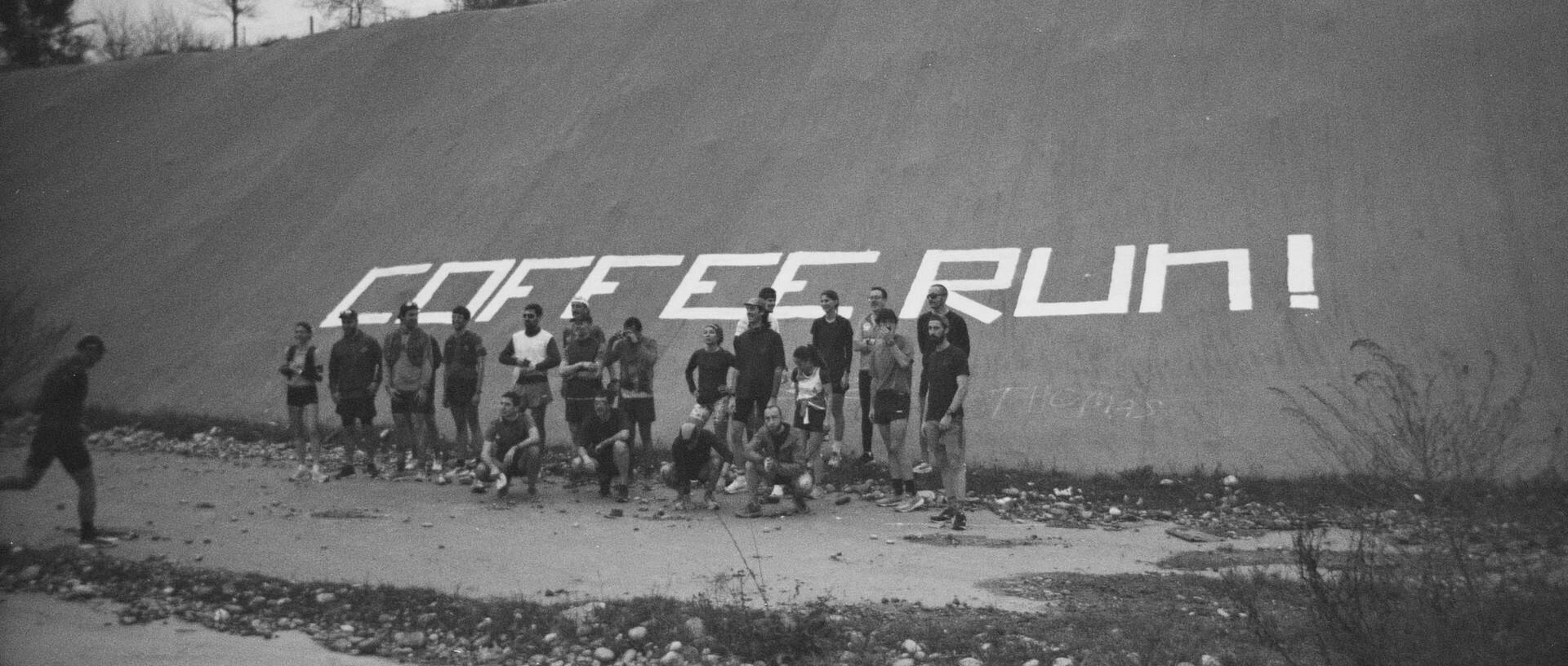 Eine Gruppe von Personen vor einem Hügel auf dem COFFEE RUN! in Großbuchstaben geschrieben ist.