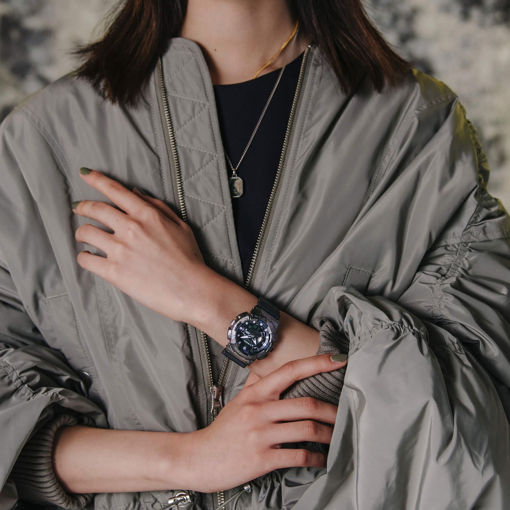 Eine Frau trägt eine graue Jacke und greift sich ans Handgelenk, dort trägt sie eine runde, analoge Armbanduhr mit lilanen Details aus der 40th Anniversary Sonderedition "Adventurer's Stone"