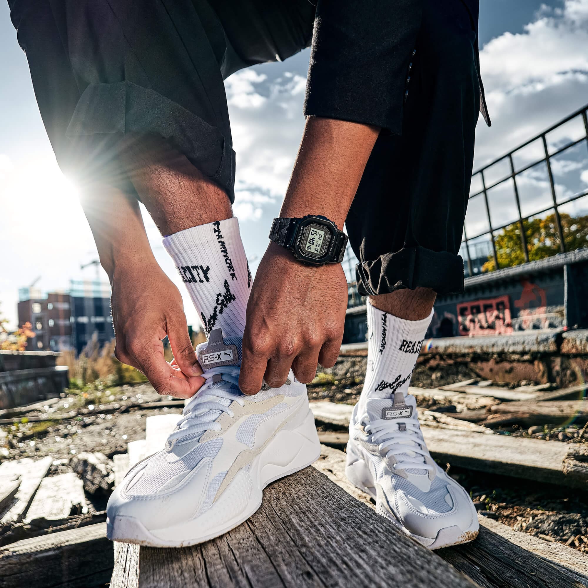 Die schwarze Digitaluhr "GMW-B5000EH-1ER" in Kollaboration mit dem New Yorker Designer Eric Haze am Handgelenk eines Mannes, der sich seine weißen Sneaker zubindet.