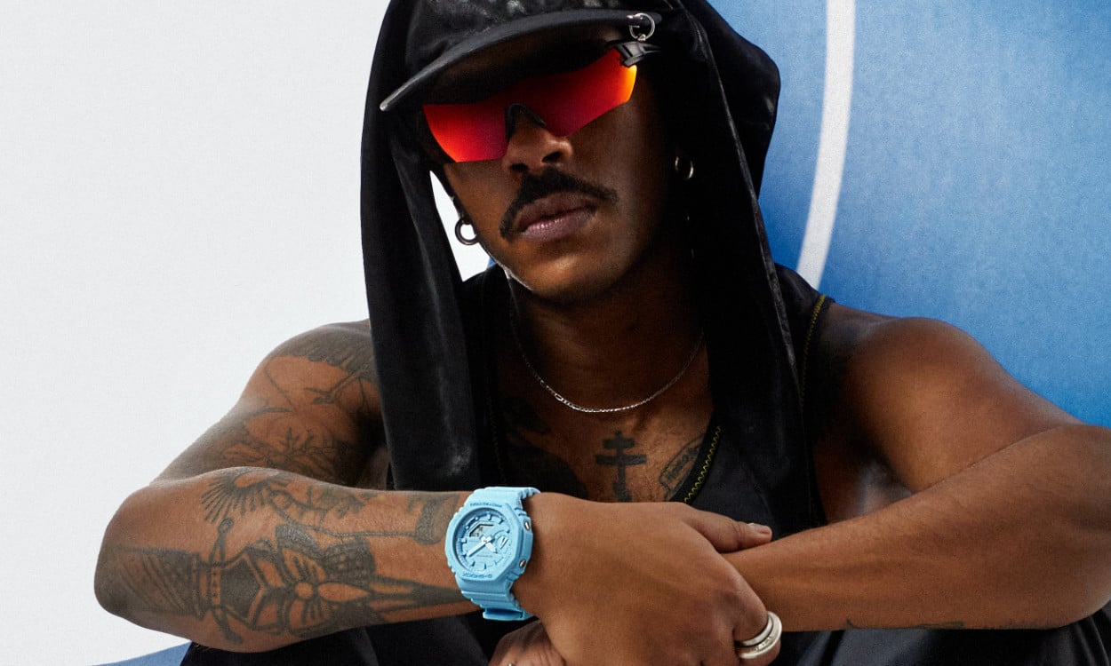 G-SHOCK "Tone on Tone" Modell in hellblau am Handgelenk, der Mann sitzt auf einer blauen Laufbahn und trägt eine Sportsonnenbrille