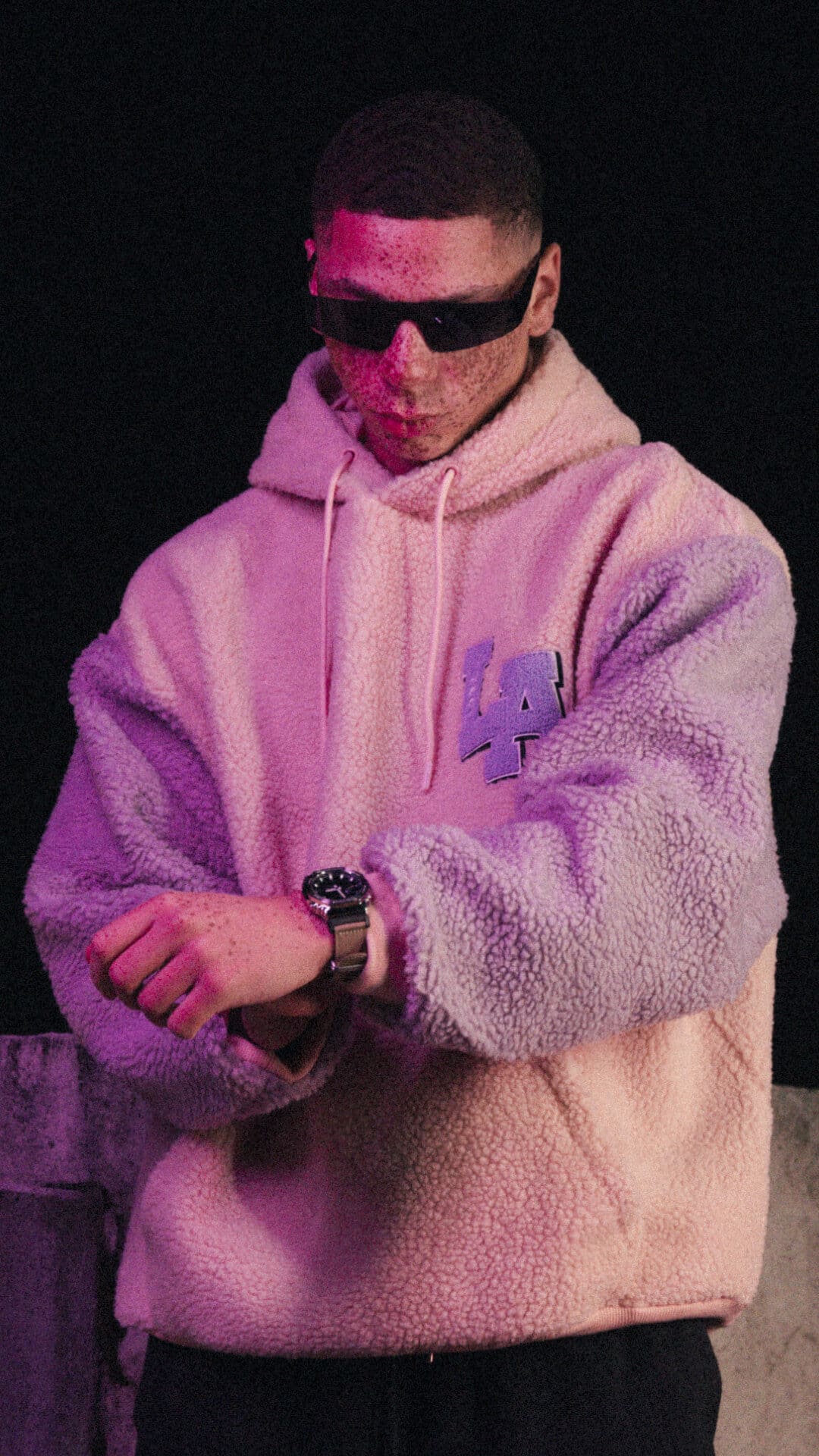 Ein Mann mit Sonnenbrille und weißem Pullover zieht sich die G-SHOCK Uhr mit Stoffarmband in beige an