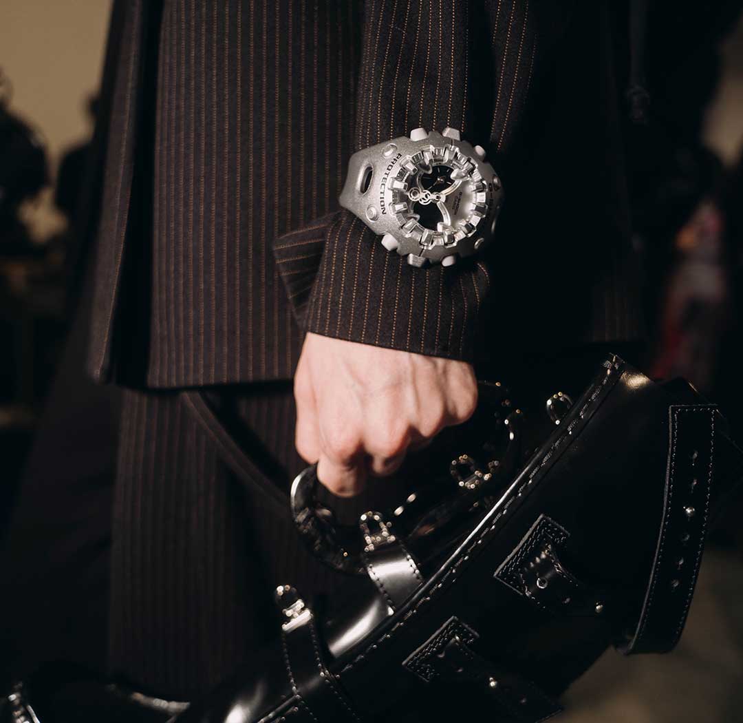 Eine Frau im Nadelstreifenanzug trägt eine schwarze Handtasche und die silberne, analog-digitale 'GA-V01' Armbanduhr