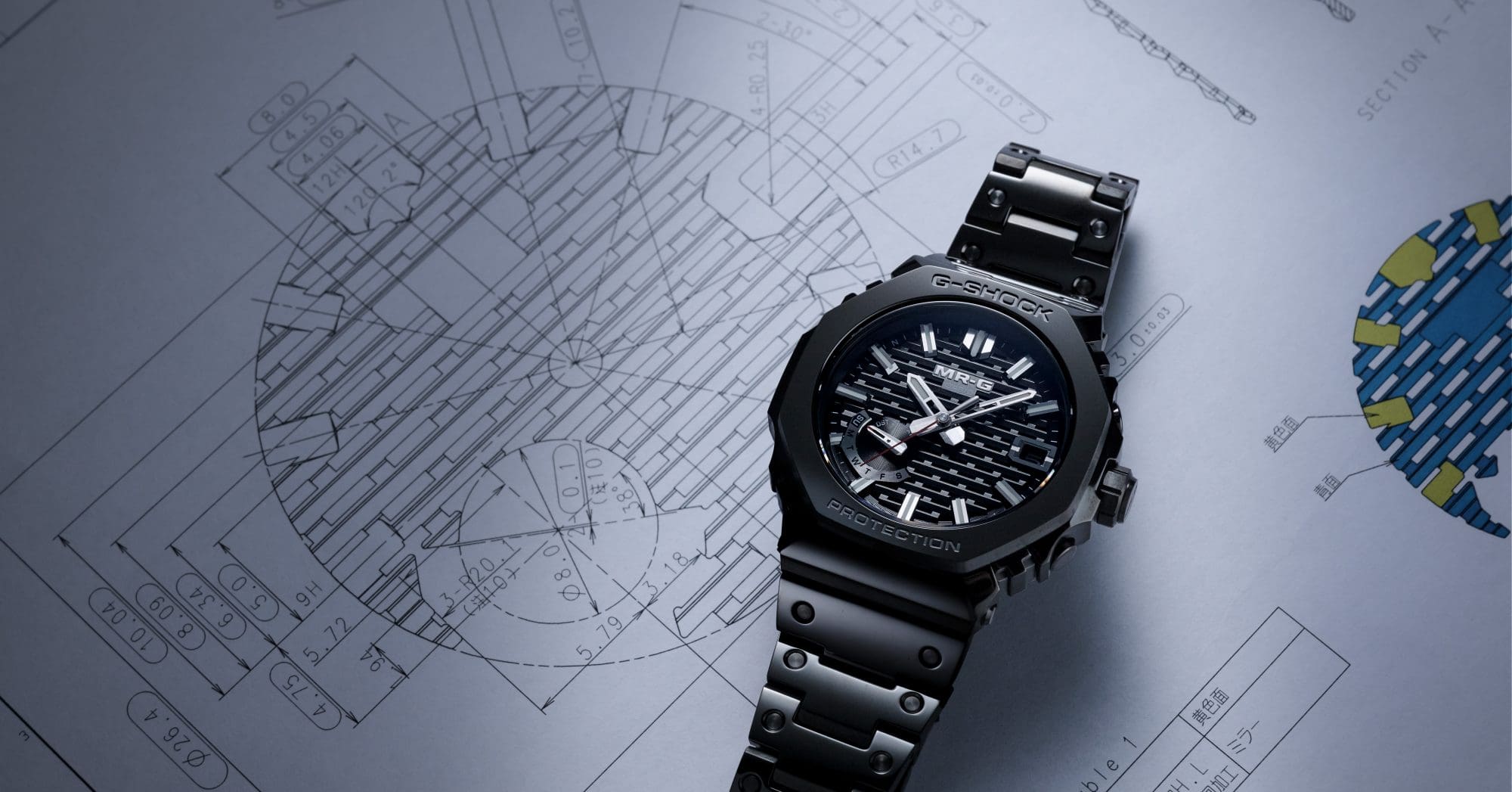 Die MR-G B2100B mit schwarzem Armband und schwarzen Zifferblatt liegt auf einer technischen Zeichnung der Uhr.