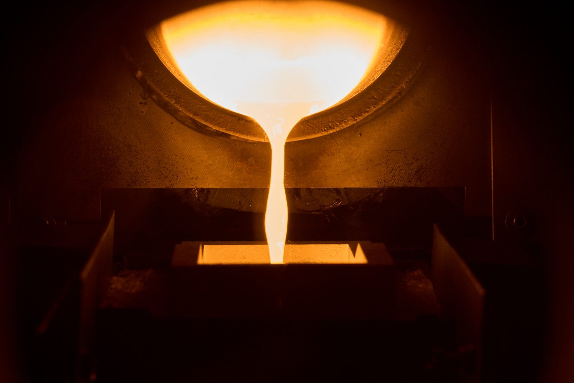 Flüssiges, glühendes Metall fließt aus einem Schmelztiegel in eine Form