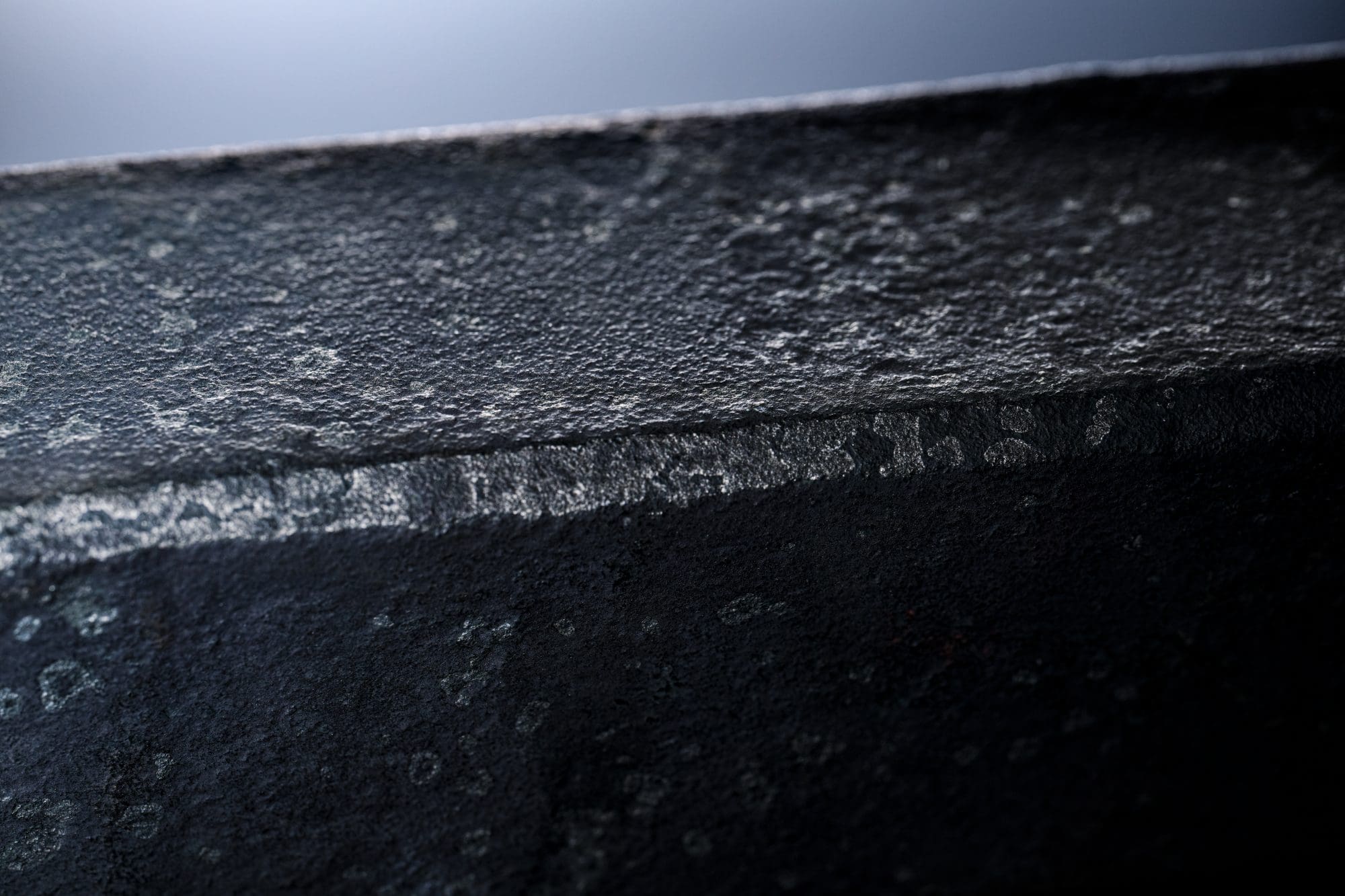 Nahaufnahme einer dunklen, rauen Metalloberfläche mit sichtbarer Struktur.