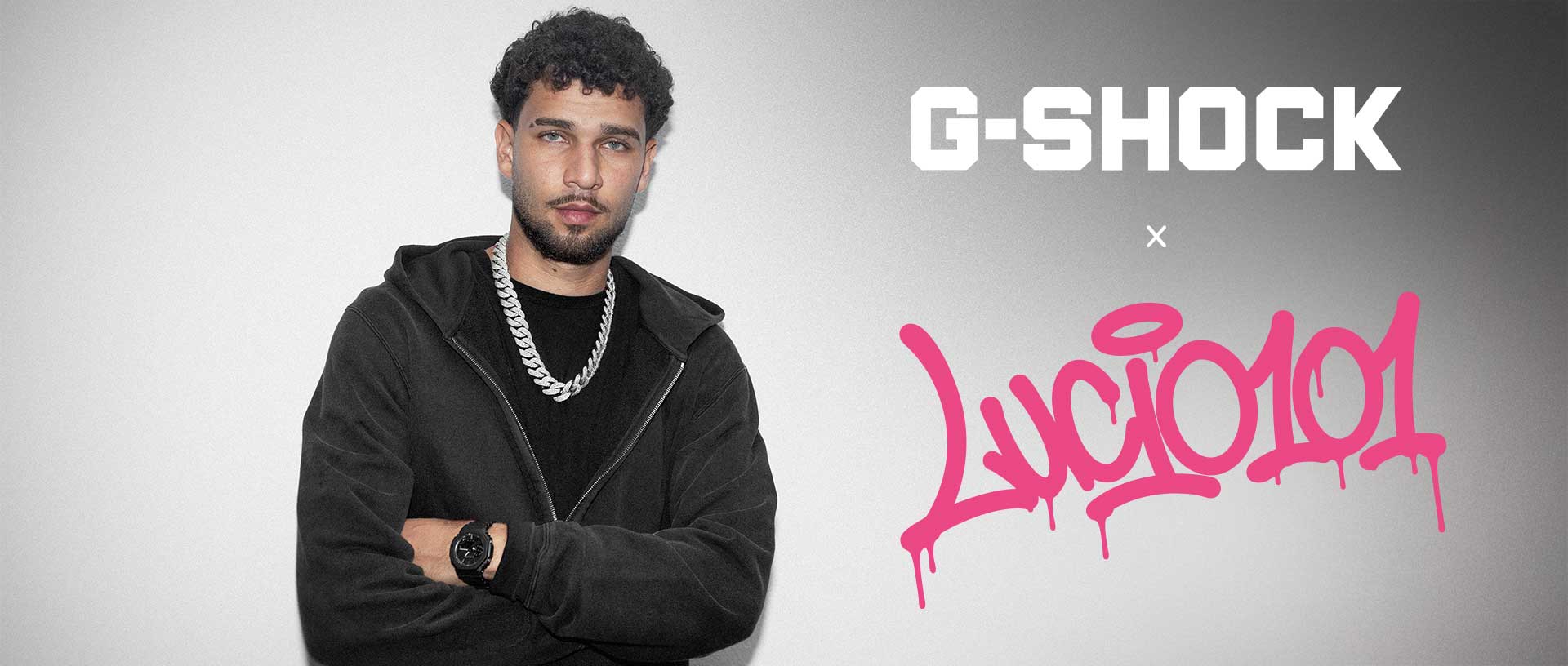 Der Rapper Lucio101 steht mit verschränkten Armen vor einer grauen Wand und trägt eine schwarze Sweatjacke. Am Handgelenk trägt der die schwarze G-SHOCK "luxe black" Armbanduhr GA-2100LXB.