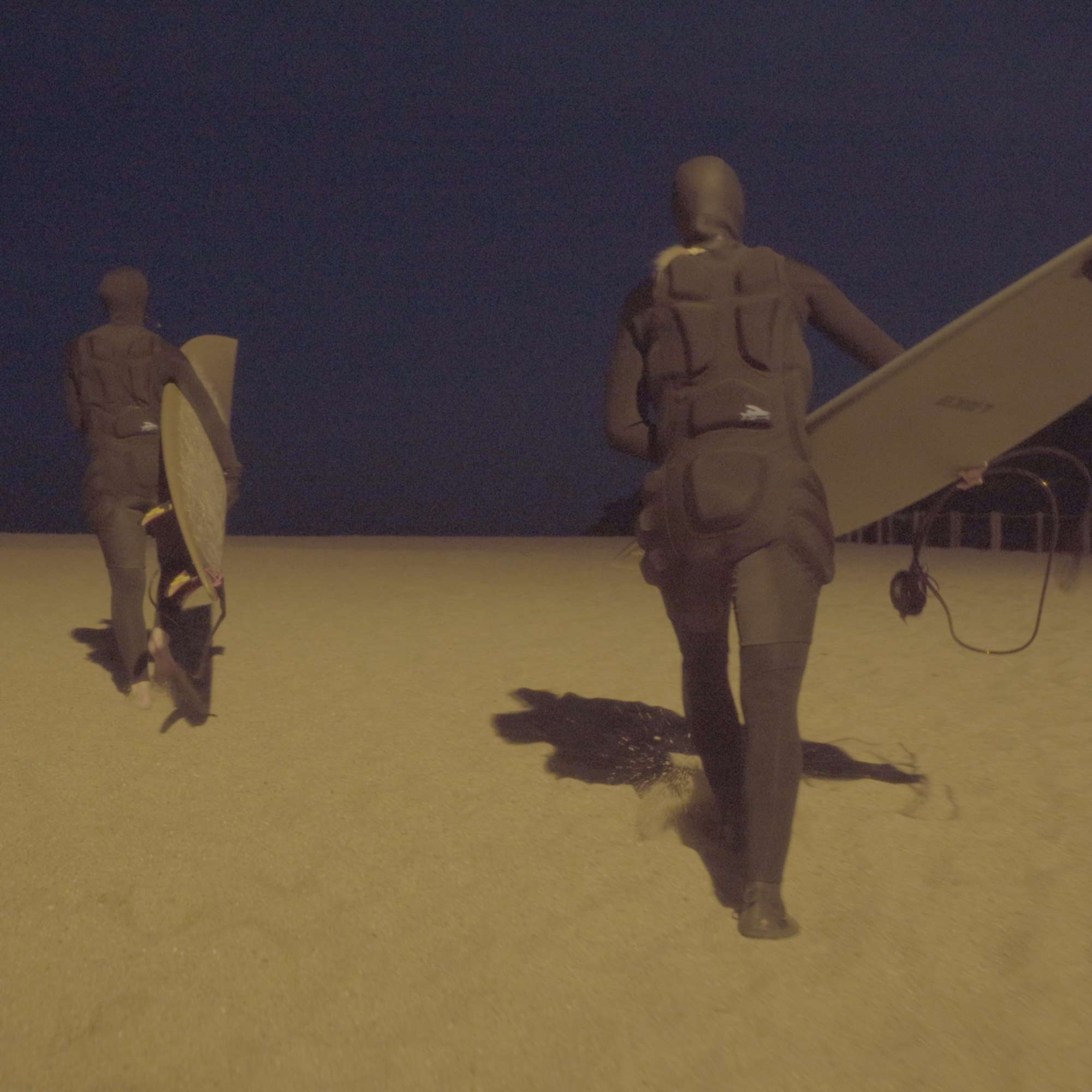 Lena Kemna und Christina Gindl gehen in Neonpren-Anzug und mit Surfboard am Strand entlang.