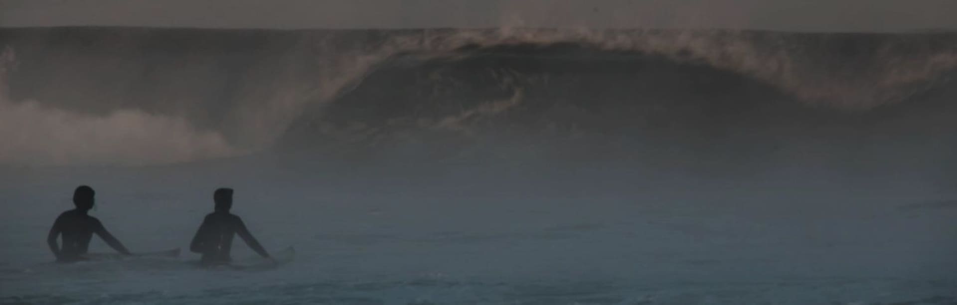 Lena Kemna und Christina Gindl sitzen auf Surfboards im Wasser vor einer Welle