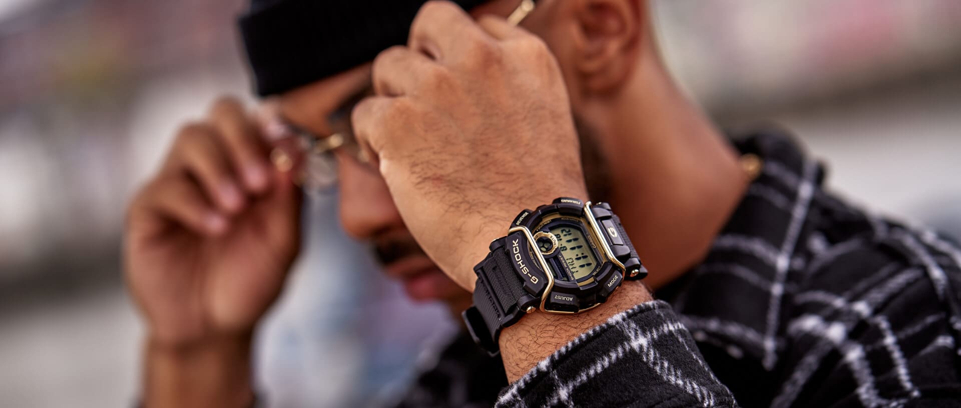 Halbtotale eines Mannes, der seine Brille aufsetzt, am Handgelenk trägt der die G-SHOCK Uhr "GD-400GB-1B" mit runder Digitalanzeige, schwarzem massivem Gehäuse und schwarzem Resinband. Am Gehäuse ist ein goldener Bügel.