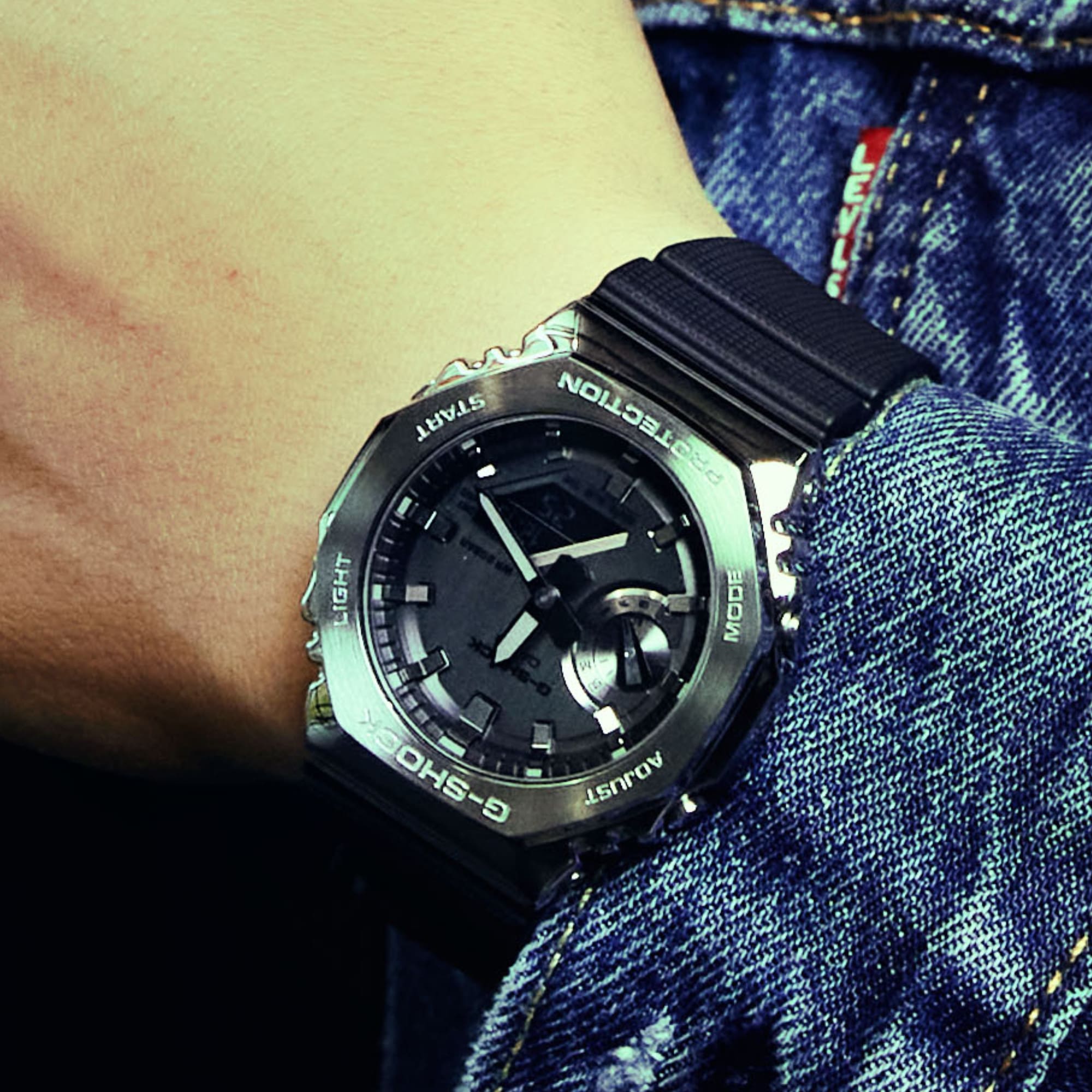 Die analoge Armbanduhr GM-2100-1A mit schwarzem Resinarmband und metallenem, achteckigem Gehäuse am Handgelenk einer Person, die eine Jeansjacke trägt.