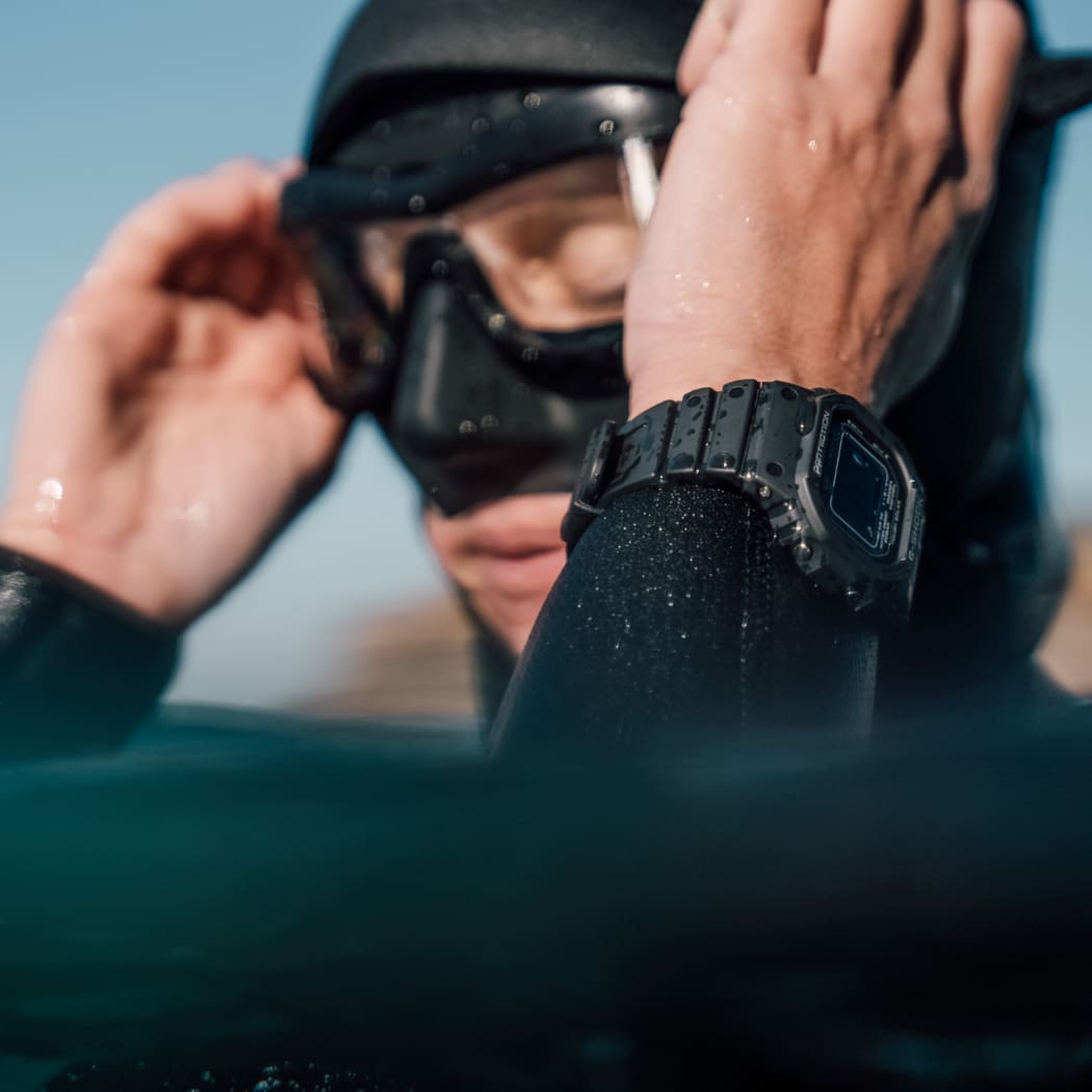 Nahaufnahme einer Frau, die einen Neoprenanzug und eine Taucherbrille trägt. An ihrem Handgelenk trägt sie die schwarze Digitaluhr GW-5000.