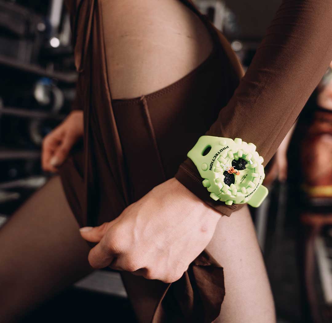 Nahaufnahme einer Frau auf dem Laufsteg in brauner Kleidung, die die GA-V01 Armbanduhr von G-SHOCK in Neongelb am Handgelenk trägt
