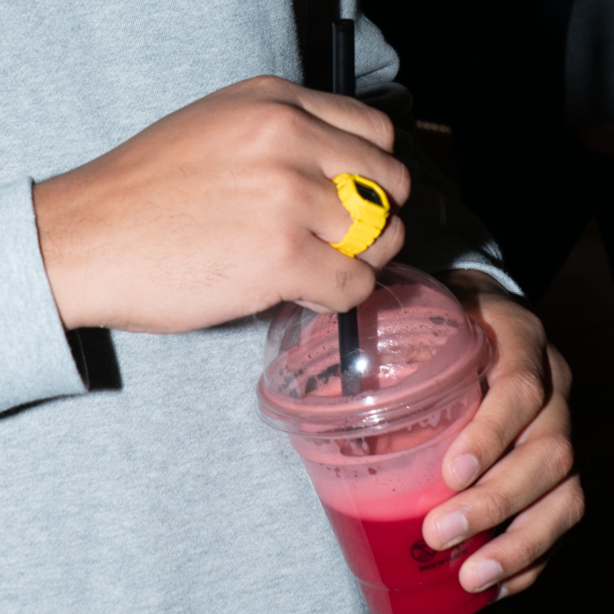 Nahaufnahme der Hände eines Mannes, der einen roten Smoothie in der Hand hält und die gelbe digitale Ringuhr trägt.