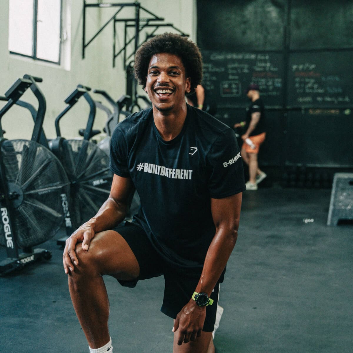 Un hombre hace estocadas en el gimnasio. Sonríe a la cámara y lleva el reloj deportivo G-SQUAD de G-SHOCK.