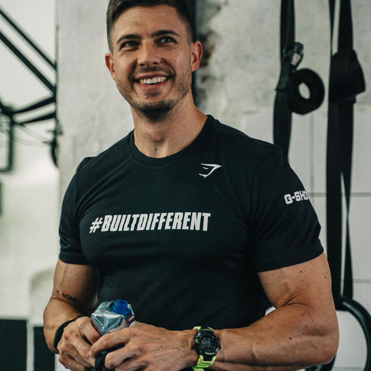 Un miembro del equipo del estudio de Crossfit sonríe a la cámara. Lleva un agua en la mano y en el brazo se ve el GBD-H2000 de G-SHOCK.
