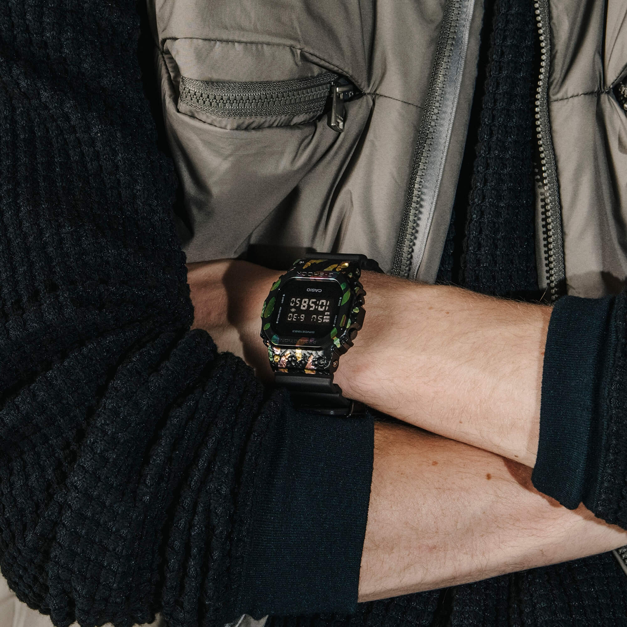 Una modelo lleva en la muñeca el reloj de pulsera G-SHOCK GM-5640GEM-1 de la edición especial «Adventurer's Stone» con correa de resina negra, caja rectangular de colores y pantalla digital.