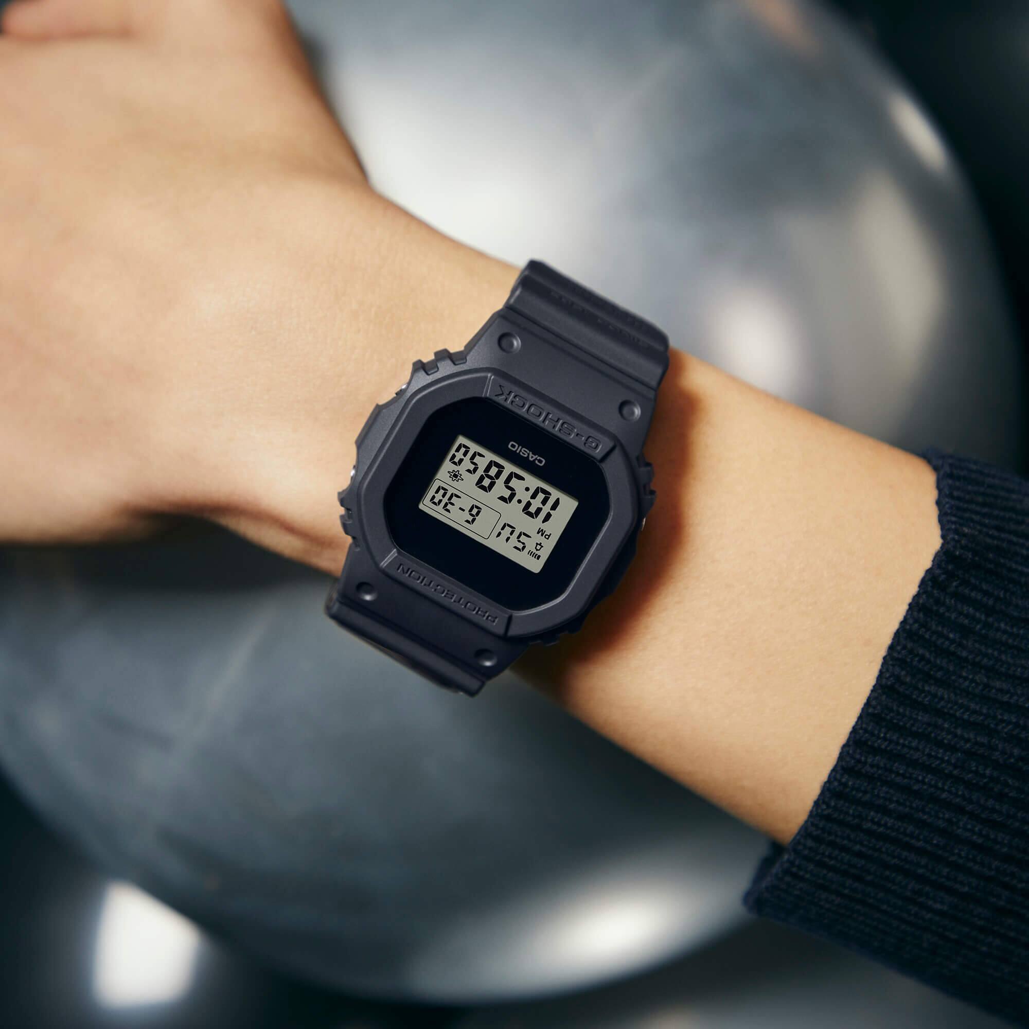 El reloj digital rectangular negro «DWE-5657RE-1» de G-SHOCK en la muñeca de un hombre.