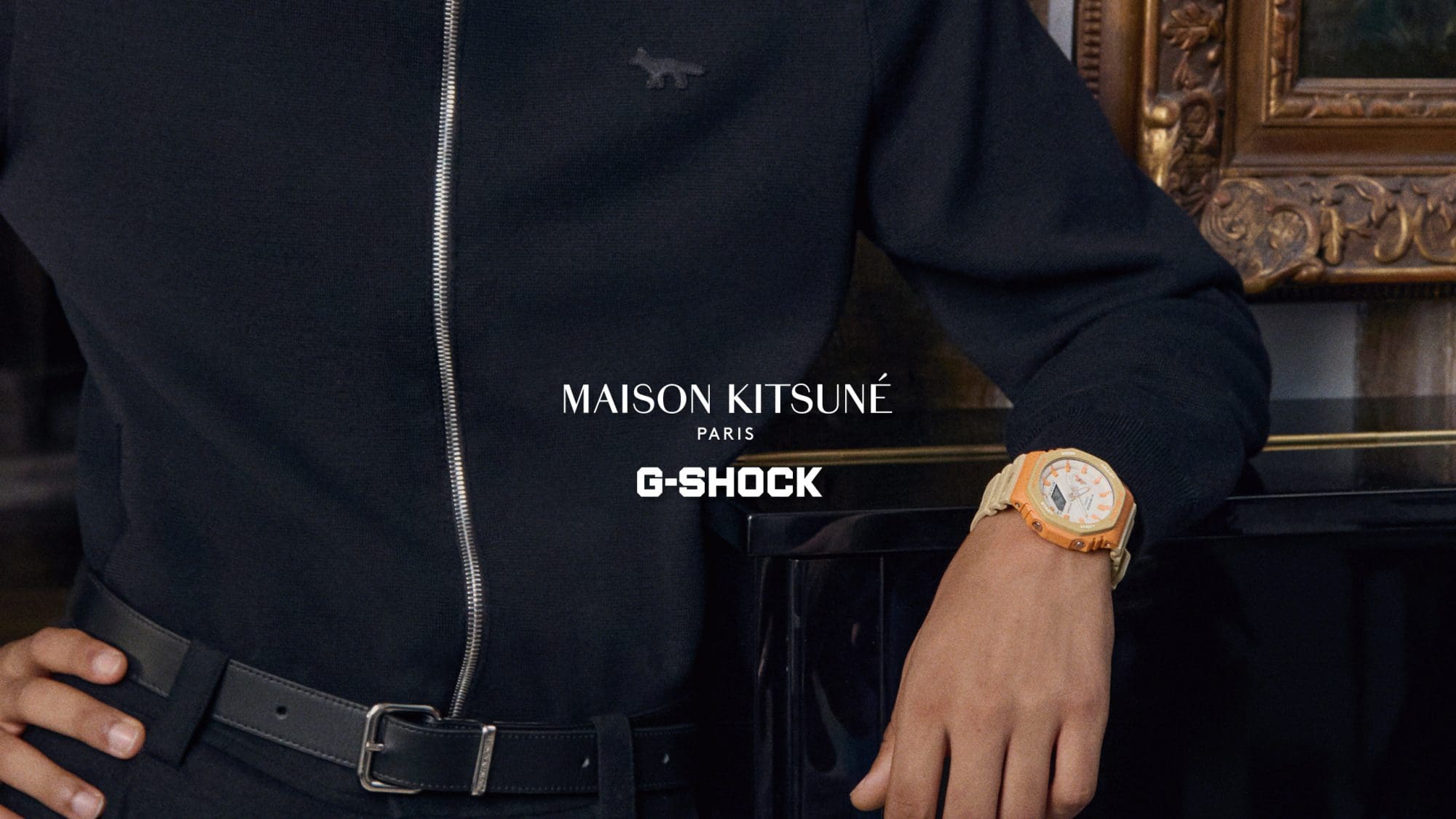 Un hombre con un cárdigan azul de Maison Kitsune y el G-SHOCK GA-2100MK-5A beige/naranja en la muñeca se apoya en un piano