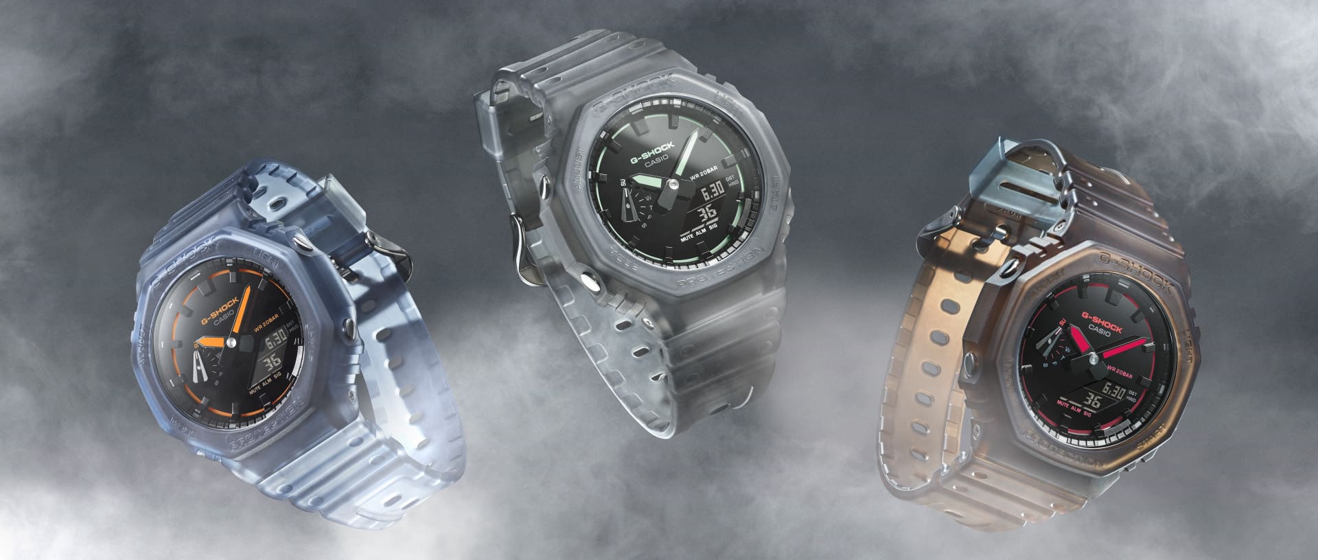 Three G-Shock GA-2100K wristwatches in different colours with analogue-digital octagonal displays and transparent straps float side by side in the mist.