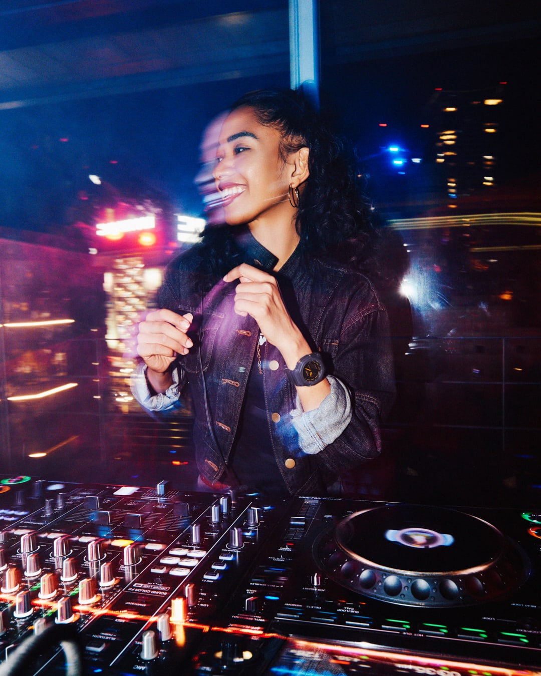 A smiling, dancing woman behind a DJ booth. She is wearing the analogue-digital Casio G-Shock GA-2100K-2A on her wrist.