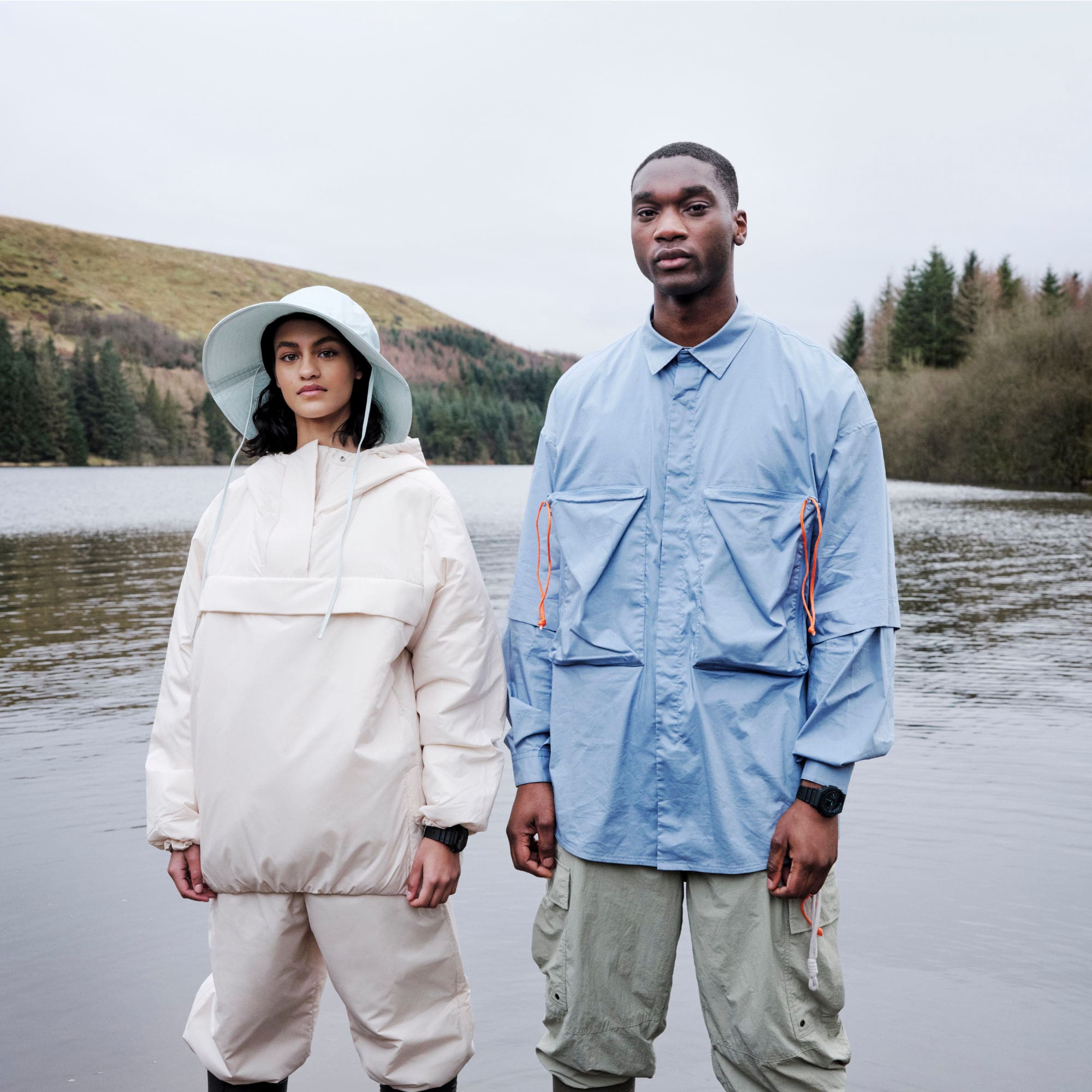 Two people wear variants of the G-SHOCK Utility Black. In the background, you can see a lake and mountains