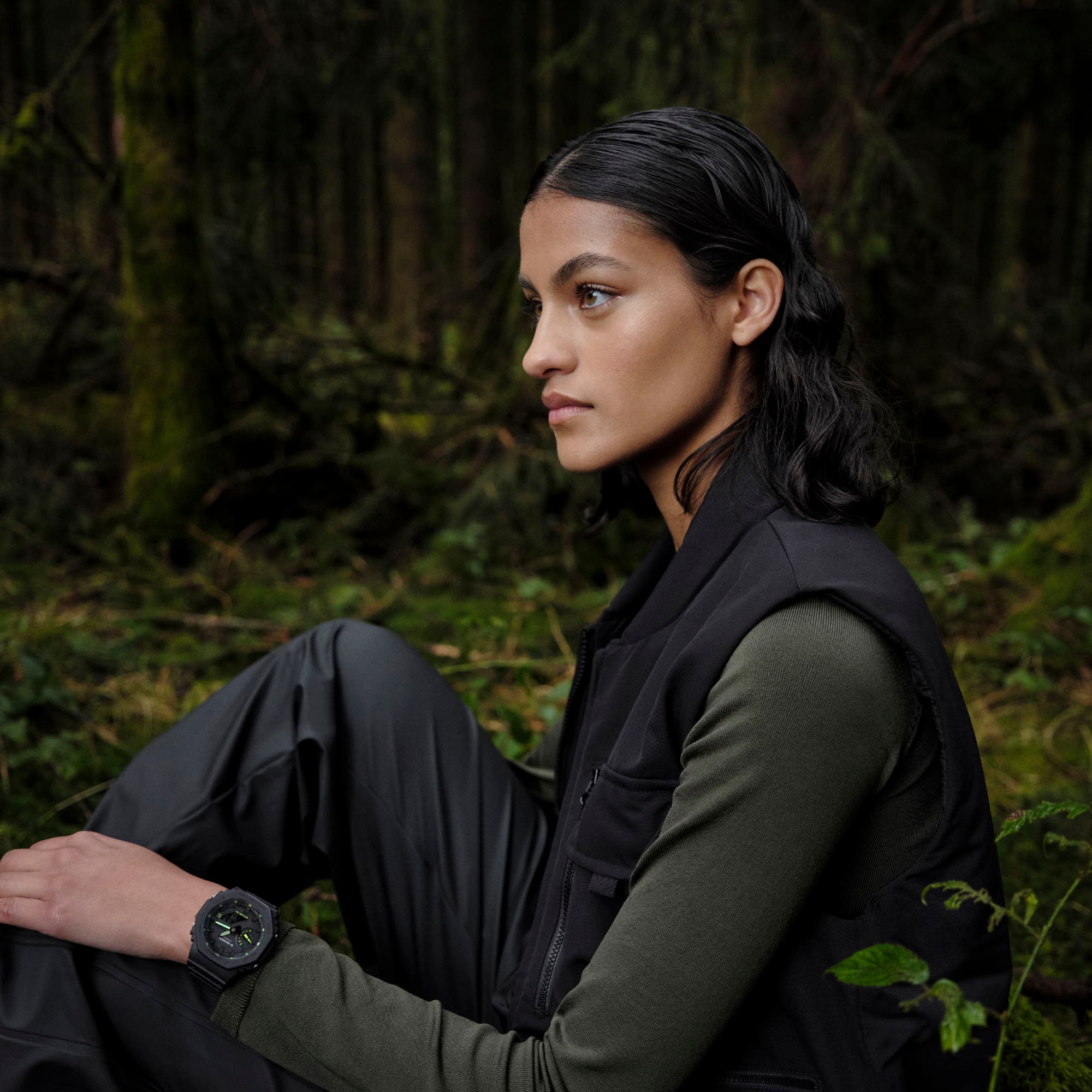 A woman sits in the forest wearing the watch model G-SHOCK GA-2100-1A3.