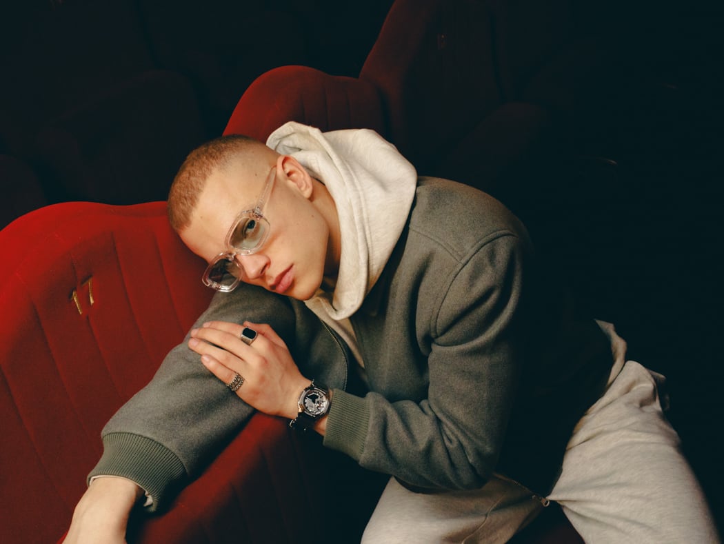A young man leans over a red armchair in an empty cinema and wears the GM-2100YM-8AER.