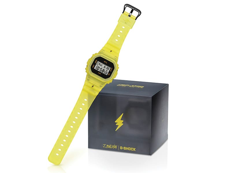 The yellow J.Balvin wristwatch next to its grey transparent packaging