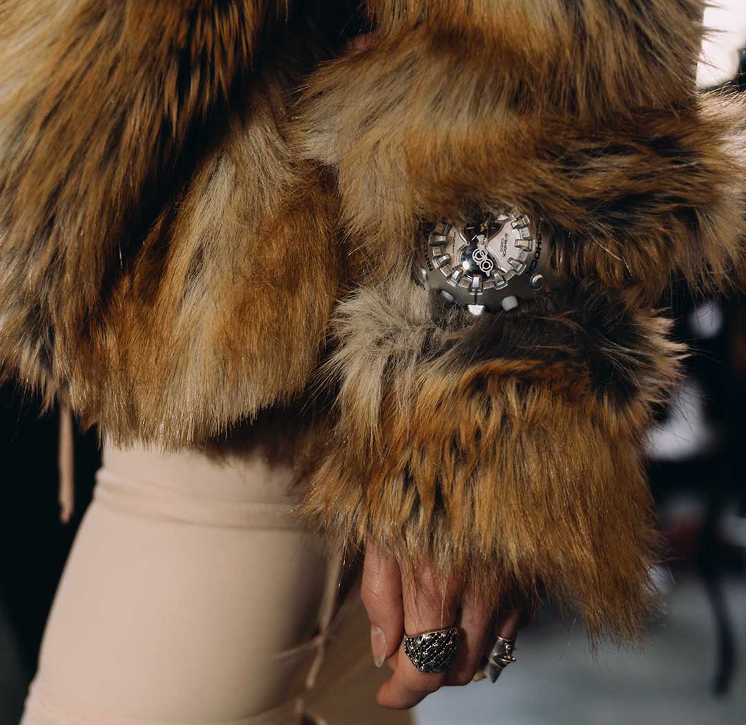 A woman in a plush, light brown jacket wears the massive G-SHOCK GA-V01 wristwatch in silver on her wrist