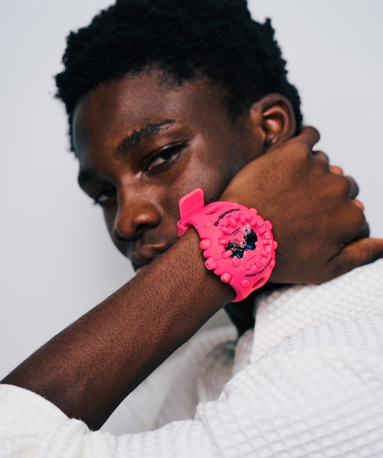 A model looks into the camera and touches her neck, wearing the bright pink GA-V01 with an analogue dial on her wrist.