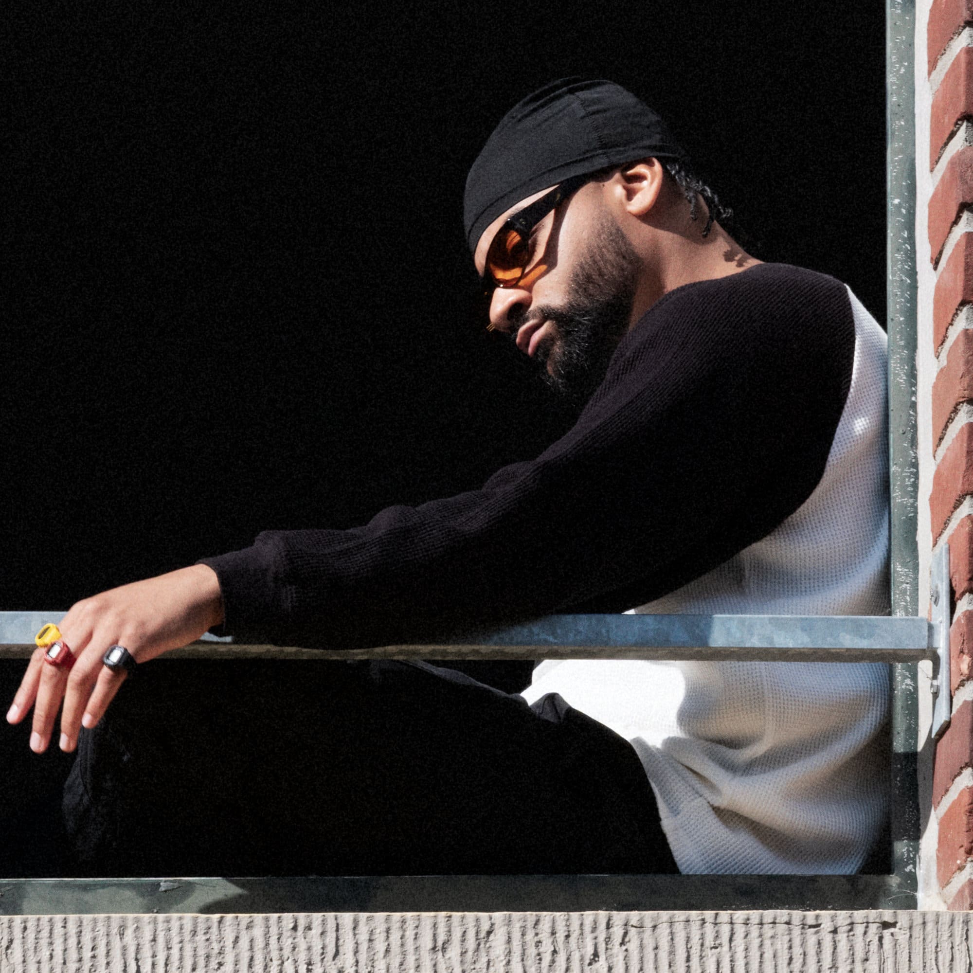 The male model is sitting and leaning on a brick wall looking down. He is wearing all three colorways of the CASIO Ringwatch on his fingers: black, red and yellow