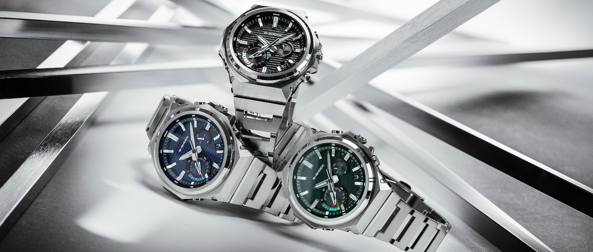 The three GST-B1000 analogue watches with black, dark blue and dark green bezel stacked on top of each other in front of a white brackground.