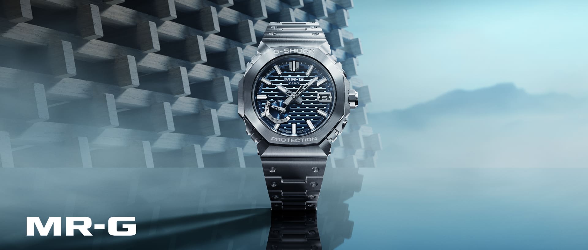 The G-Shock MRG-B2100D-2A with a silver band and an analoge blue patterned bezel in front of a light blue background