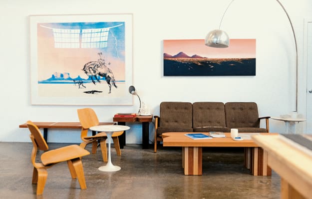 L'espace d'accueil dans l'atelier de l'artiste McCormick, avec un canapé, des chaises et une table. Au mur, deux de ses tableaux. L'image renvoie vers l'interview du créateur Matt McCormic.