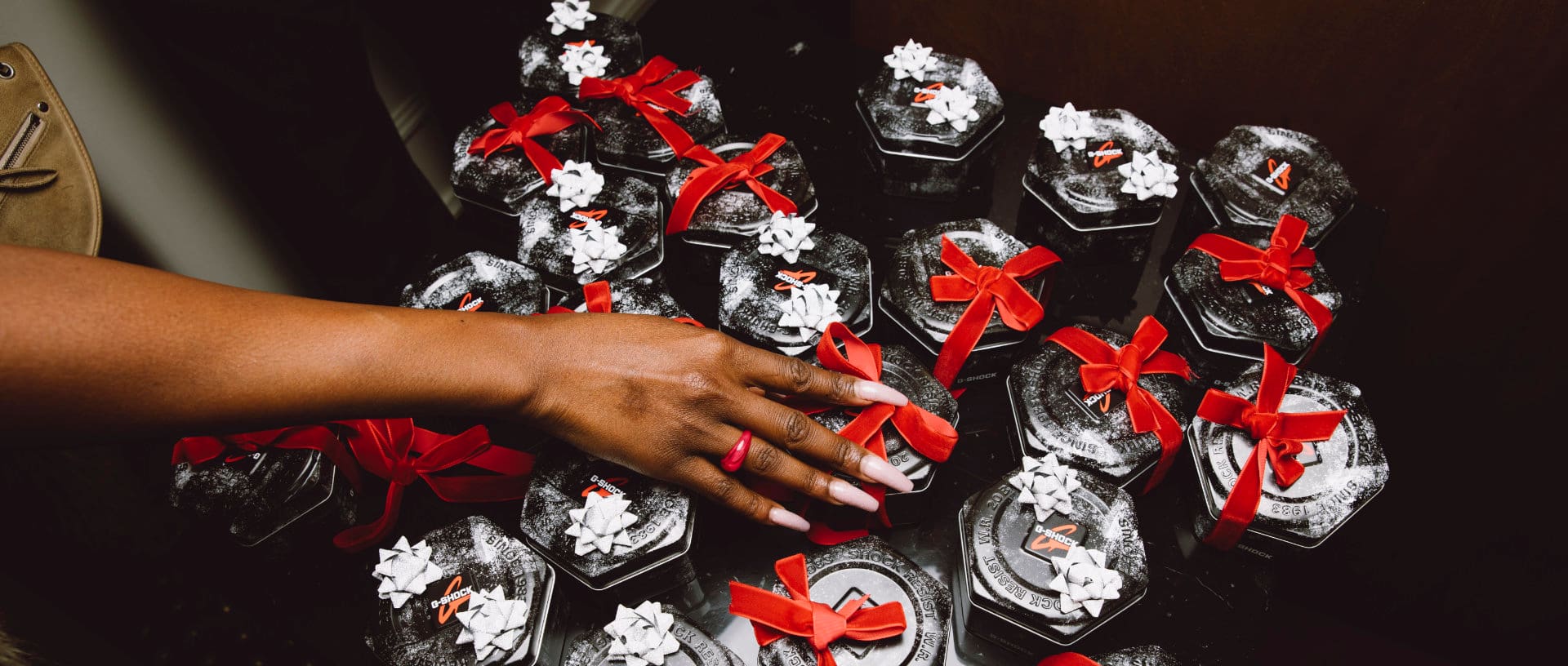 Plusieurs emballages de montres G-SHOCK sont posés sur une table avec un ruban cadeau, une femme saisit l'une des montres.