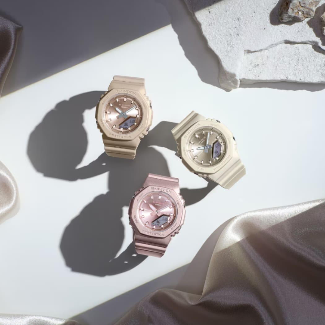 Trois montres-bracelets de la série GMA-P2100 de G-SHOCK sur une table avec des bracelets de couleur mate en marron clair, beige et rose.