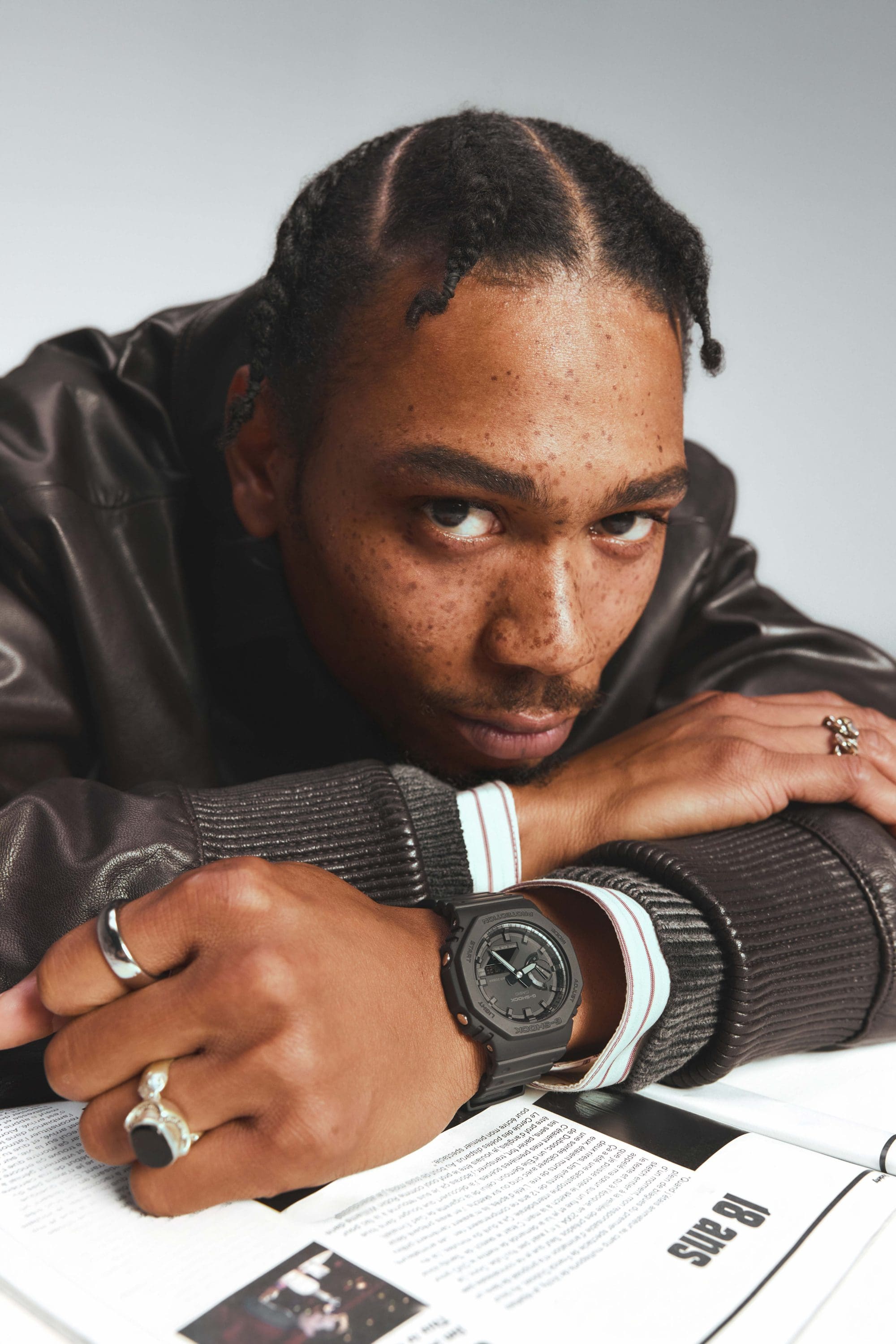 Un homme pose sa tête sur ses bras sur une table, il regarde directement la caméra. Il porte au poignet la G-SHOCK GA-2100 noire.