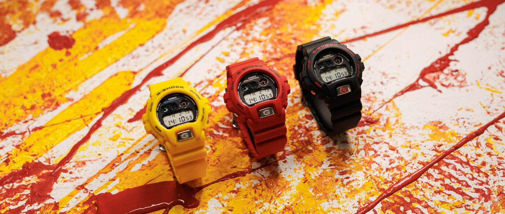 Les versions jaunes, rouges et noires de la montre DW-6900TR posées sur un sol coloré.