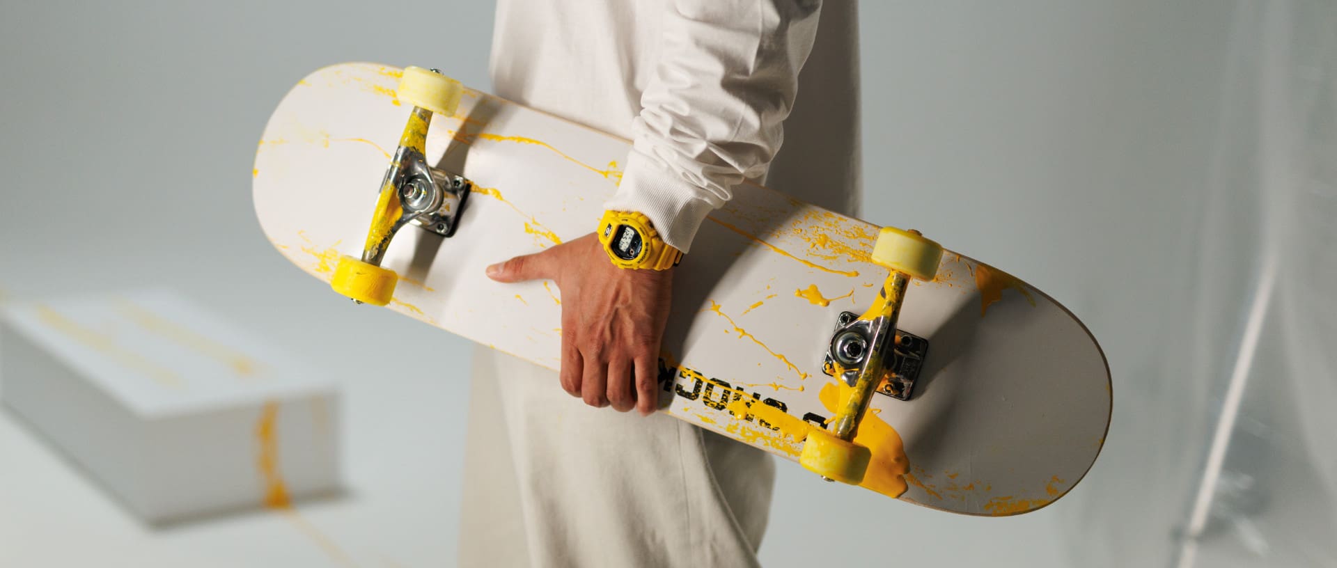 Un homme tient son skateboard et porte la version jaune de la montre numérique G-SHOCK DW-6900TR-1ER.