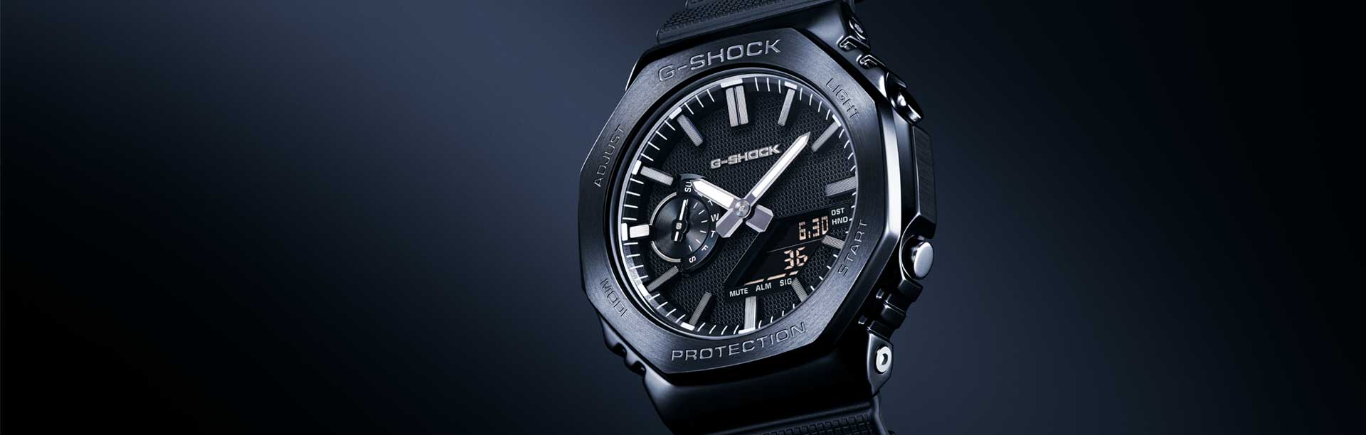 Montre analogique-numérique G-Shock GM-2100LXB-1A noire avec boîtier octogonal, cadran noir et bracelet résistant en résine sur fond sombre.
