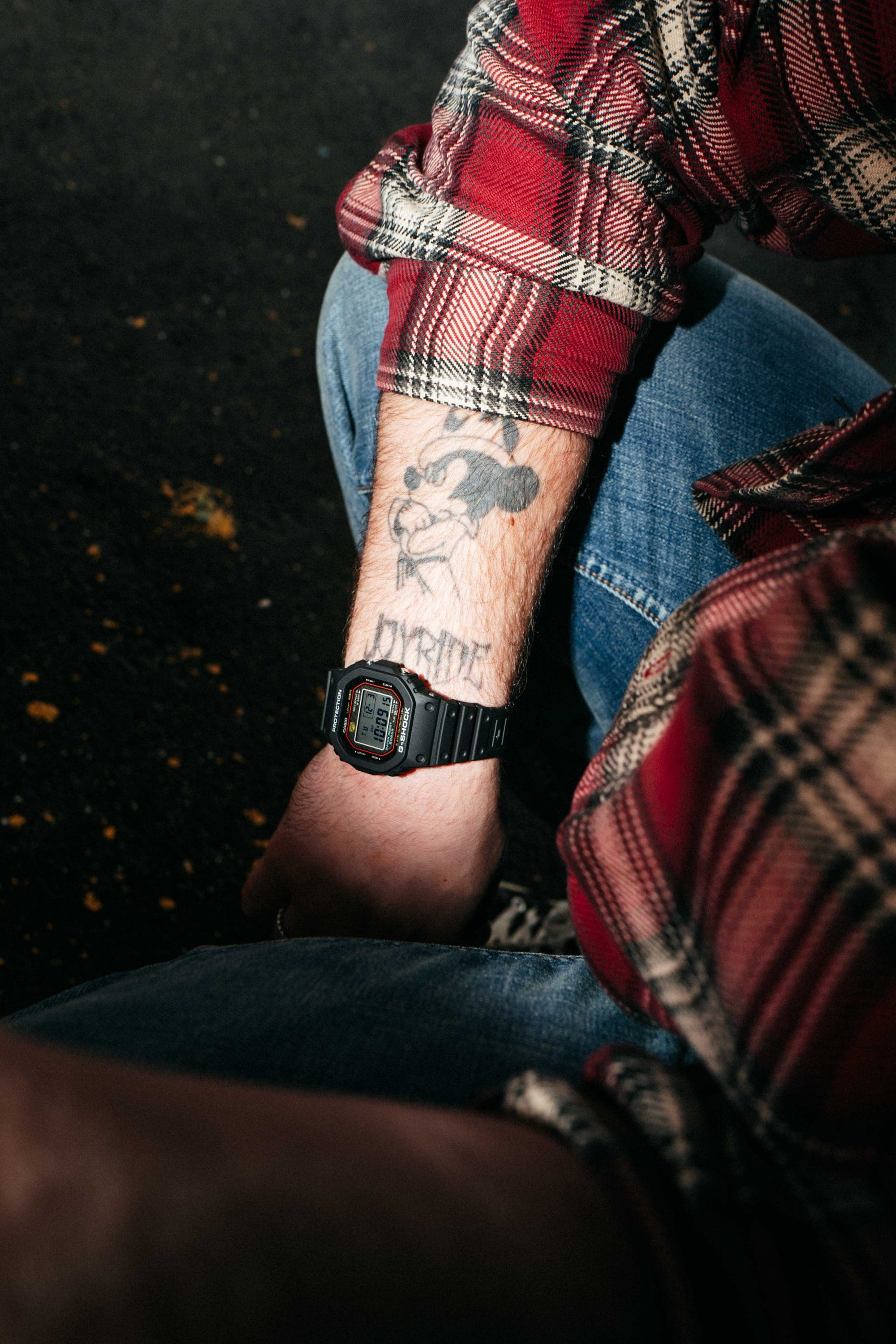  La G-SHOCK DW-5000R noire au poignet d'un skateur en chemise à carreaux rouges