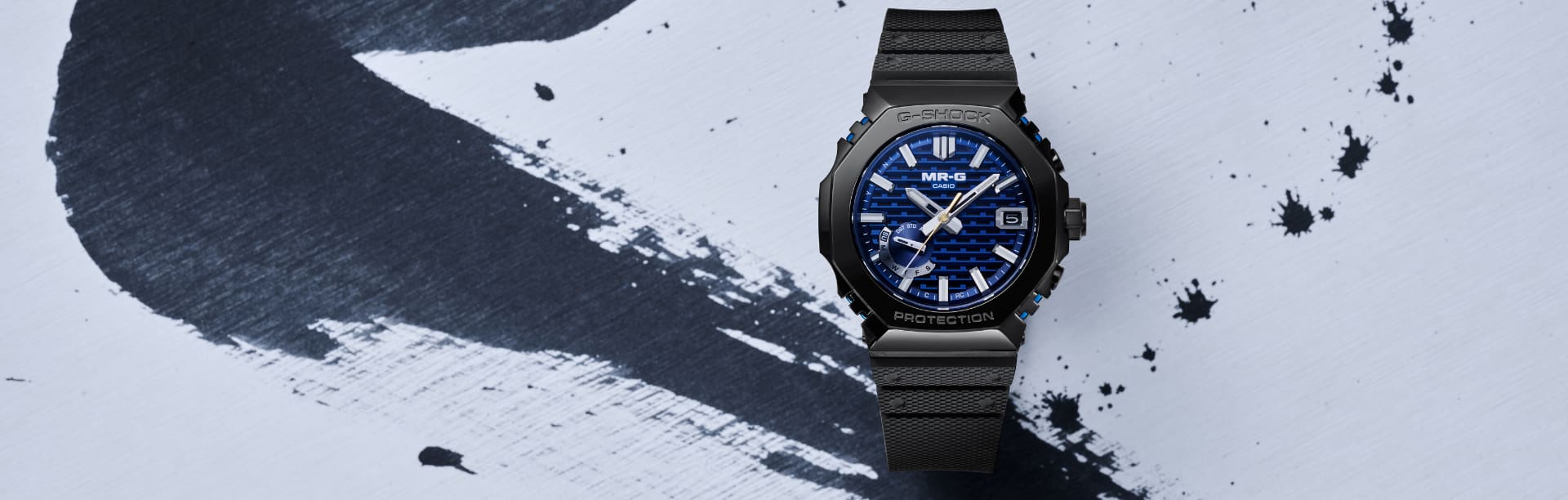 Le MRG-B2100R avec bracelet noir et lunette bleu nuit sur fond d'encre.