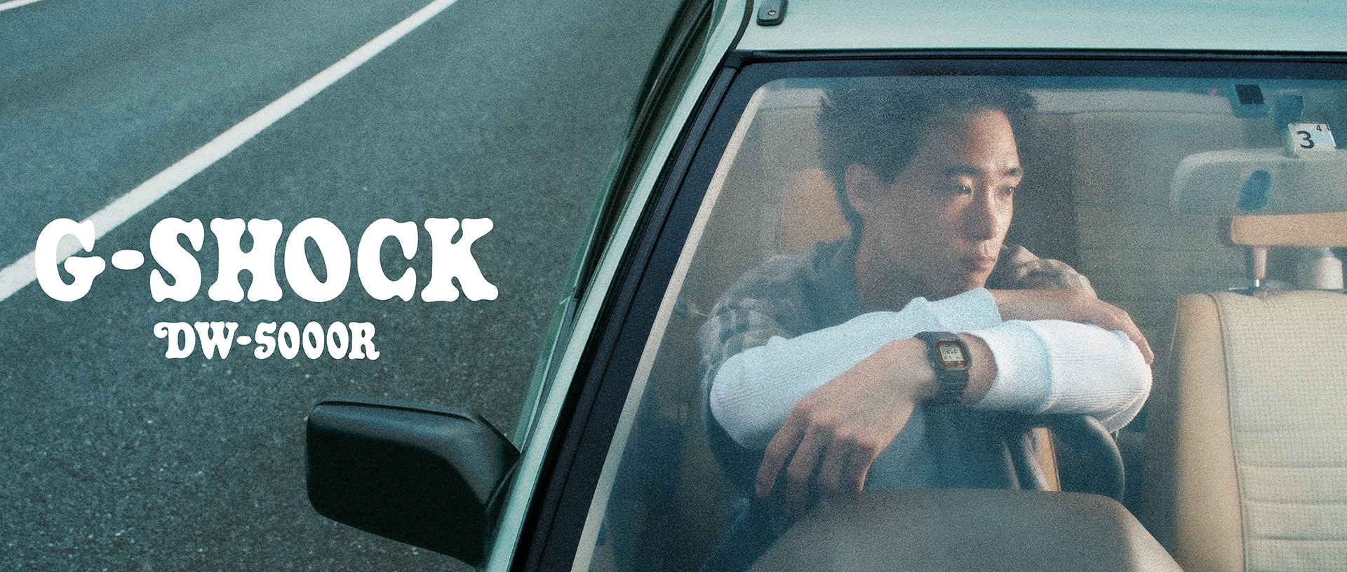 A man wearing a G-SHOCK DW-5000R watch sitting in a car.