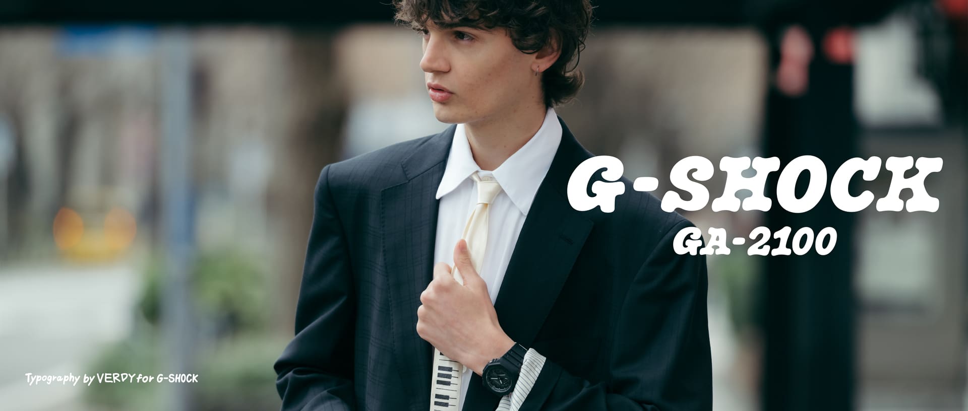 Person in suit adjusting tie wearing G-SHOCK GA-2100 in an urban setting.